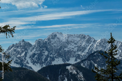 Scenic view of snow capped mountain peaks of Karawanks on the way to Sinacher Gupf in Carinthia, Austria. Mount Wertatscha is visible through dense forest in early spring. Rosental on a sunny day.Hike photo
