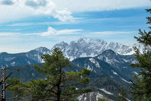 Scenic view of snow capped mountain peaks of Karawanks on the way to Sinacher Gupf in Carinthia, Austria. Mount Wertatscha is visible through dense forest in early spring. Rosental on a sunny day.Hike photo