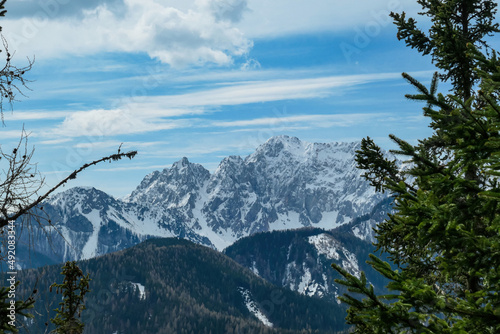 Scenic view of snow capped mountain peaks of Karawanks on the way to Sinacher Gupf in Carinthia, Austria. Mount Wertatscha is visible through dense forest in early spring. Rosental on a sunny day.Hike photo