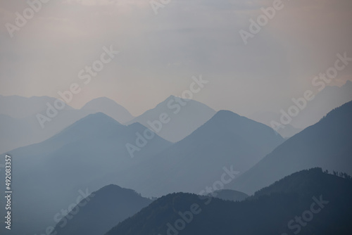 Fototapeta Naklejka Na Ścianę i Meble -  Scenic view on the alpine mountain chains of the Karawanks in Carinthia, Austria. Peaks are shrouded in morning fog. Mystical vibes. Clear and sunny day. Serenity. View from Ferlacher Spitze, Alps