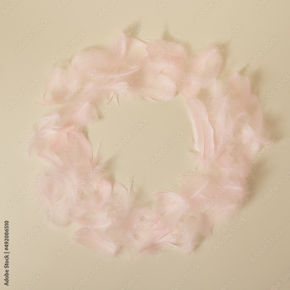 Wreath of pink pastel feathers on yellow minimal background with circle copy space.