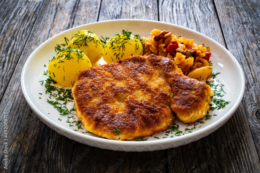 Breaded fried pork chop with boiled potatoes and cabbage on wooden table
Breaded fried pork chop with boiled potatoes and cabbage on wooden table