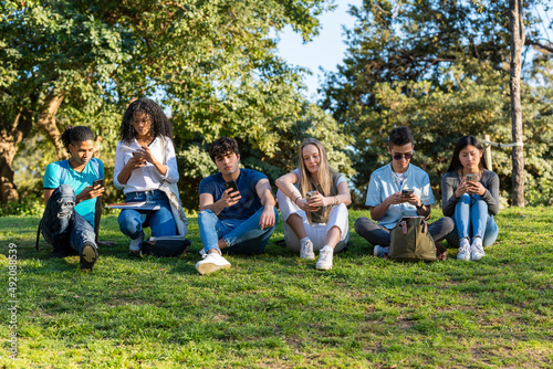 Group of teenage friends looking at the phone in the park on green grass