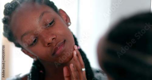 Teen girl removing acne zit in front of mirror. Black African ethnicity © Marco