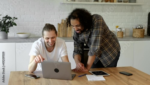 Two young guys work at home, use it in the summer and take notes, discuss a new project. Freelancers create a new application, use a computer and a tablet