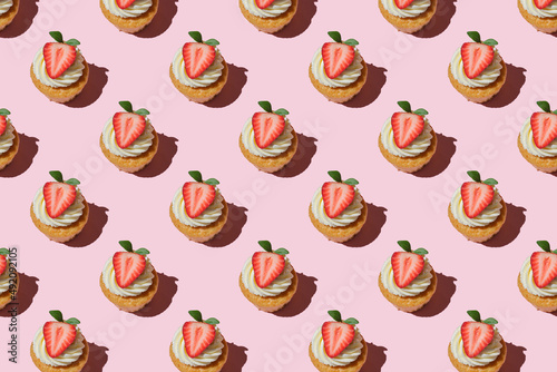 Pattern made of home cookies with strawberries and cream on a pink background. cupcake with big strawberry on top. Repeating  homemade cookies with strawberries and cream pattern. Flat lay style.
