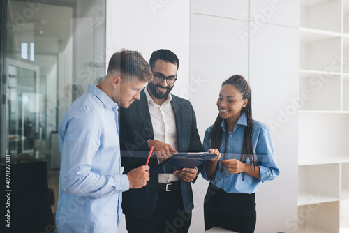 Group of cheerful experts brainstorming on ideas for capital strategy discussing information from statistics reports and smiling, happy male and female enjoying involved briefing during workday photo