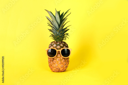 Pineapple is wearing black sunglasses and sunglasses on a blue-yellow background. Advertising accessories, summer, vacation.