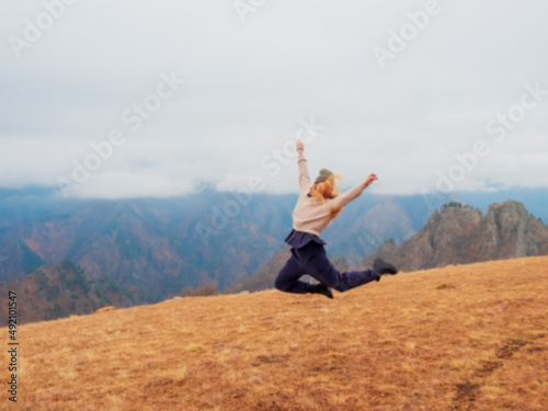 A woman jumps in an autumn field located in the highlands of the Caucasus under low overhanging clouds. Defocused photo