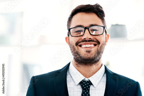 I cant help but smile when business is booming. Cropped portrait of a handsome young businessman smiling while standing in a modern office.