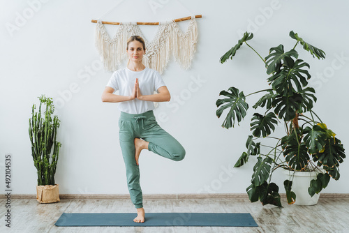 A young active girl stands on one leg with her arms connected. Practice yoga on the mat at home. Vrikshasana is a tree pose. Balance photo