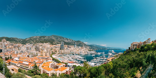 Monaco, Monte Carlo cityscape. Real estate architecture on mountain hill background. Many high-rise buildings in downtown area. Yachts moored at town quay In Sunny Summer Day.