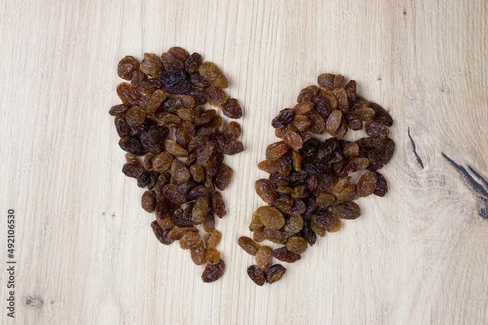 Broken heart of raisins on wooden background. Rich in fibers, provides