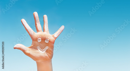 фотографія Positive symbol drawing by sunscreen (sun cream, suntan lotion) on caucasian open hand on blue sky background