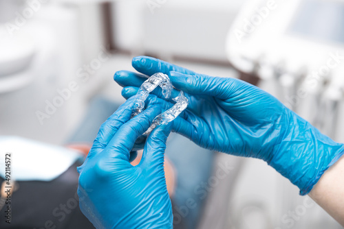 Two women hands wearing blue gloves are holding a pair of invisible aligners. photo