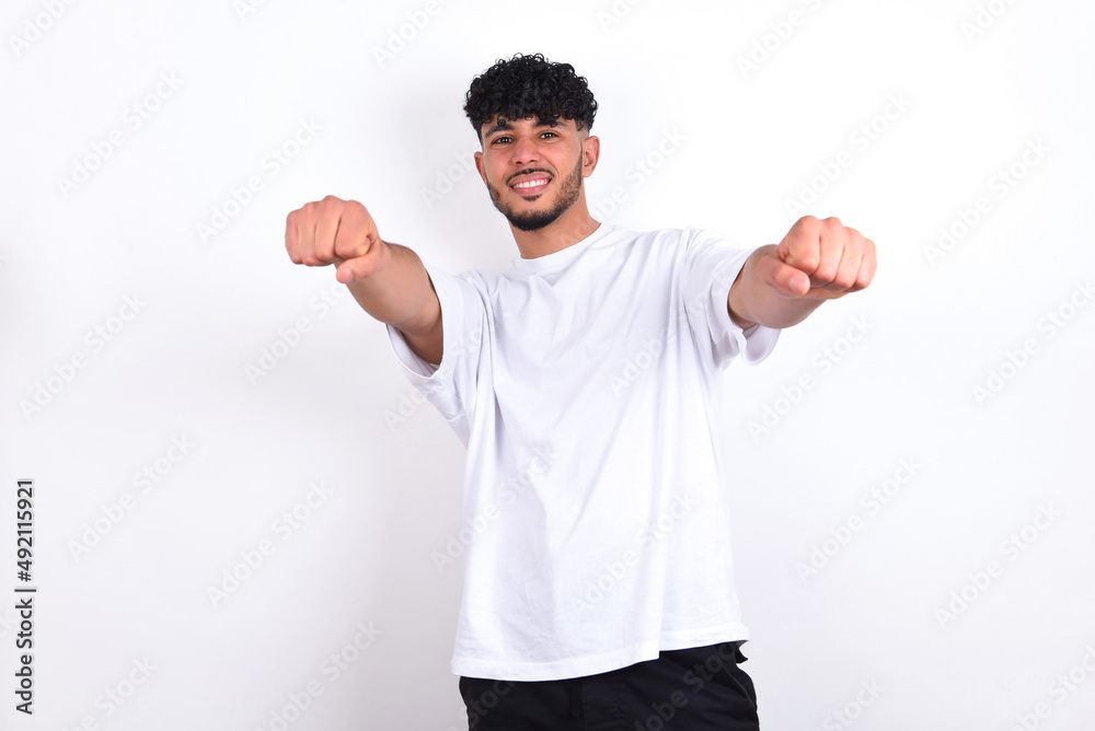Portrait of charming young arab man with curly hair wearing white t-shirt over white background , smiling broadly while holding hands over her head. Confidence and relax concept. Portrait of charming young arab man with curly hair wearing white t-shirt over white background , smiling broadly while holding hands over her head. Confidence and relax concept.