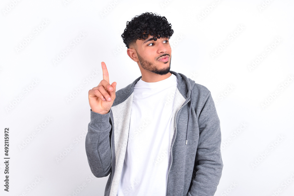 No sign gesture. Closeup portrait unhappy young arab man with curly hair wearing casual clothes over white background raising fore finger up saying no. Negative emotions facial expressions, feelings. No sign gesture. Closeup portrait unhappy young arab man with curly hair wearing casual clothes over white background raising fore finger up saying no. Negative emotions facial expressions, feelings.