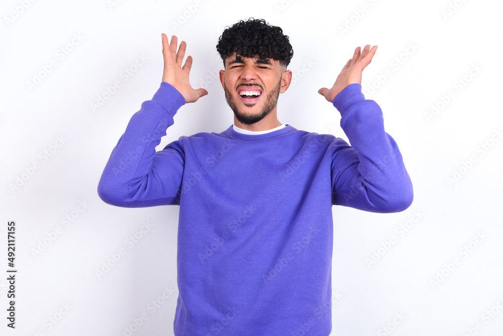 young arab man with curly hair wearing purple sweatshirt over white background goes crazy as head goes around feels stressed because of horrible situation