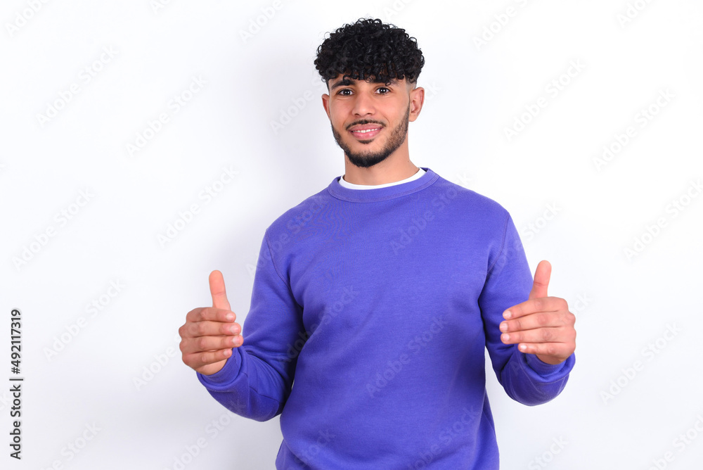 Happy young arab man with curly hair wearing purple sweatshirt over white background Holding Empty Paper Board Advertising Offer Text Standing. Autumn Advertisement Banner. Happy young arab man with curly hair wearing purple sweatshirt over white background Holding Empty Paper Board Advertising Offer Text Standing. Autumn Advertisement Banner.