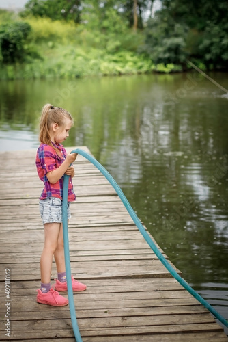 A blonde girl stands on a wooden pier on the river bank.