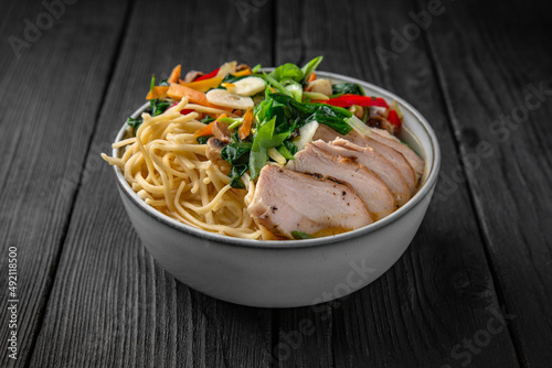 Soba Noodles in broth with chicken fillet, vegetables: carrots, sweet peppers, broccoli on a black background. Sushi menu. Japanese food