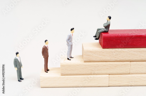 Figures of people rise on wooden blocks. At the top on the red block sits a figurine of a corrupt official photo