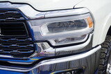 Radiator grille with headlight unit full of shiny chrome, white heavy pickup truck.
