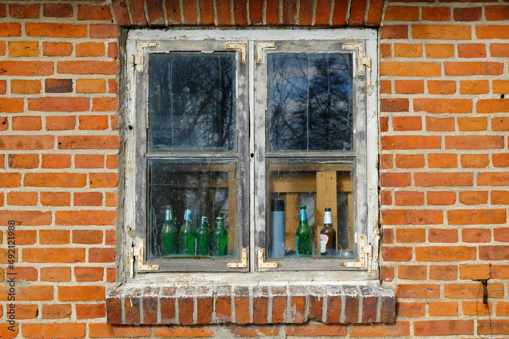 Close up of old window in brick wall of building. There are empty bottle of beer behind dirty window.