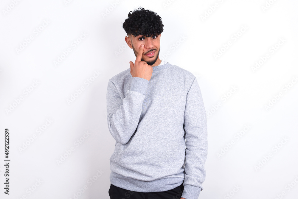 young arab man with curly hair wearing sport sweatshirt
over white background Pointing to the eye watching you gesture, suspicious expression. young arab man with curly hair wearing sport sweatshirt
over white background Pointing to the eye watching you gesture, suspicious expression.