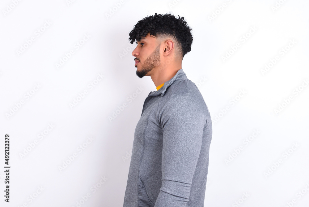 young arab man with curly hair wearing sport clothes over white background looking to side, relax profile pose with natural face with confident smile. young arab man with curly hair wearing sport clothes over white background looking to side, relax profile pose with natural face with confident smile.