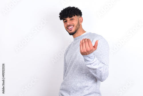 young arab man with curly hair wearing sport sweatshirt over white background inviting to come with hand. Happy that you came