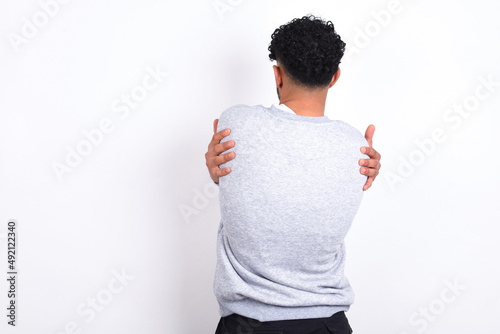 Cuadro en lienzo young arab man with curly hair wearing sport sweatshirt
over white background hugging herself happy and positive from backwards