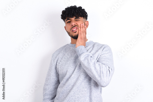 Fotografie young arab man with curly hair wearing sport sweatshirt
over white background touching mouth with hand with painful expression because of toothache or dental illness on teeth