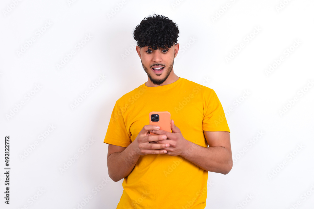 young arab man wearing yellow T-shirt over white background using mobile phone chatting free time . young arab man wearing yellow T-shirt over white background using mobile phone chatting free time .