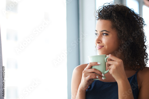 Its going to be such a good day. Shot of an attractive young woman holding a coffee mug and looking out the window in the morning.