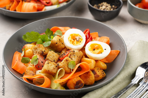 Sweet potato gnocchi with teriyaki tofu with indonesian vegetable salad gado gado - carrots, cucumbers, tomatoes, coriander, sesame seeds, boiled eggs and peanut butter dressing in a grey bowl
