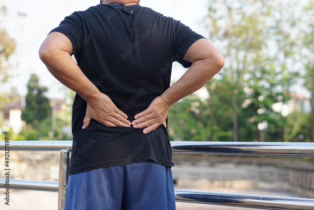 Man feels hurt his back, uses hands to massage waist. Back view