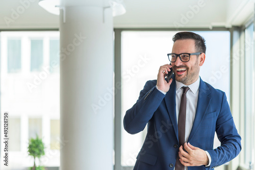 Smiling young businessman talking on the phone in his office. Portrait of successful young manager, boss, mentor