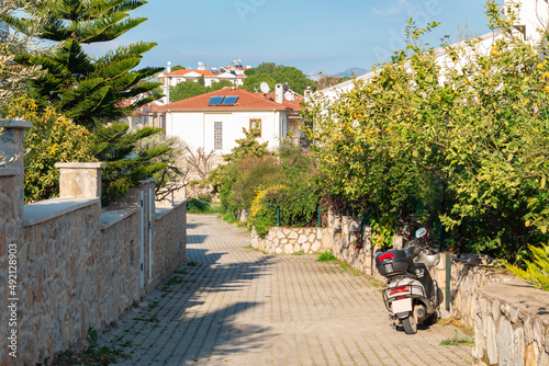 Street in Datça Turkey. White houses and green trees. There is a parked motorcycle. Touristic place.