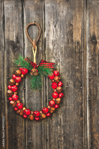 A Christmas wreath of red and brown bells hanging from a rustic hook on a wood plank wall