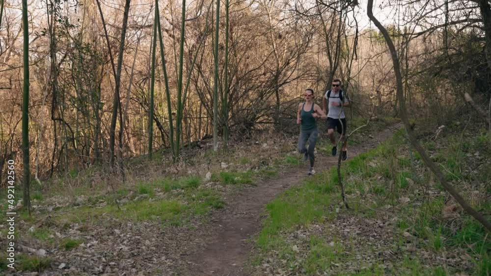 Smiling trail running couple jogs on dirt trail chasing each other through lush forest in 4k slow motion at golden hour sunset tracking backwards Smiling trail running couple jogs on dirt trail chasing each other through lush forest in 4k slow motion at golden hour sunset tracking backwards