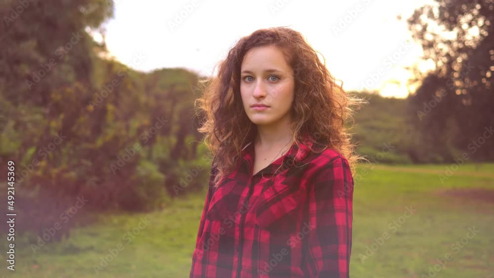 pensive young woman staring at camera at park changes expression and smiles pensive young woman staring at camera at park changes expression and smiles