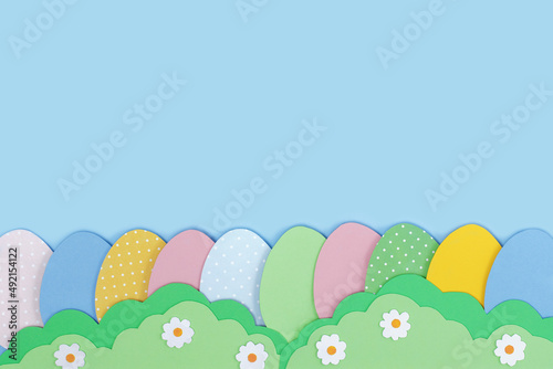 Happy Easter. Painted Easter eggs cutting out paper and grass made of green paper on blue background. Easter greeting card template. Creative easter minimal concept with copy space. Flat lay