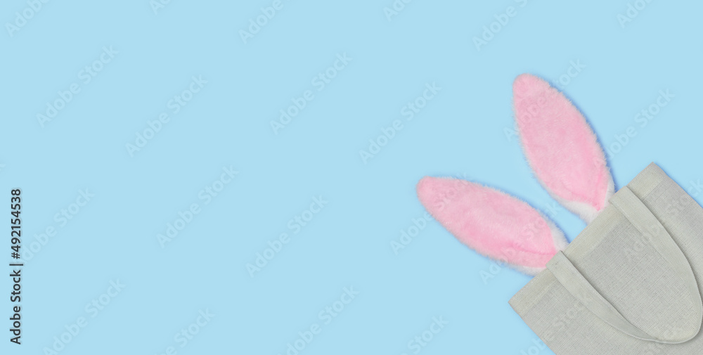 Banner. Pink Easter bunny ears sticking out of Reusable textile bag on a blue background. Happy Easter minimal concept. An Easter card with a copy of the place for the text. Flat lay