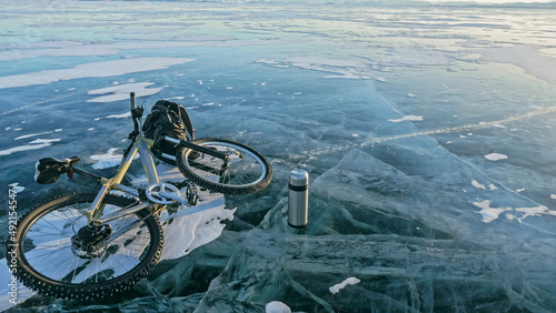Man and his bicycle on ice. He looks at the beautiful ice in the cracks. First-person view on bike. Nearby is a thermos and biking backpack. Ice of the frozen Lake Baikal.