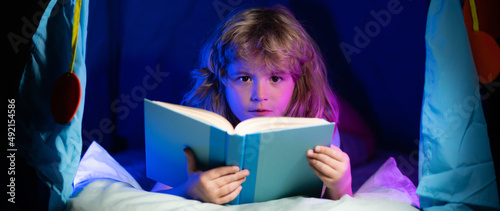 Kids reading a book in the dark home. Child boy reading a book lying on the bed. Dreaming child read bedtime stories, fairystory or fairytale. photo