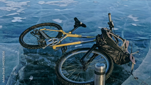 Man and his bicycle on ice. He looks at the beautiful ice in the cracks. First-person view on bike. Nearby is a thermos and biking backpack. Ice of the frozen Lake Baikal.