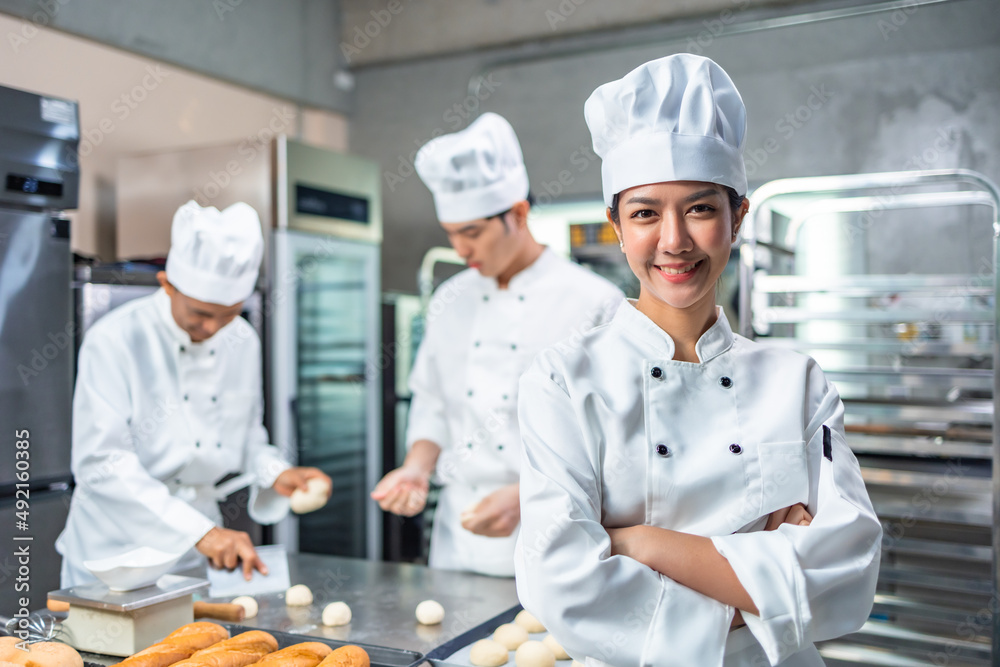 Smiling  asian  female bakers looking at camera..Chefs  baker in a chef dress and hat, cooking together in kitchen.Team of professional cooks in uniform preparing meals for a restaurant in kitchen.