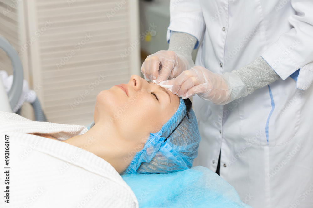Photo of professional female cosmetologist using sponges to wash the face of a woman client preparing for a cosmetic procedure. Rejuvenating and moisturizing procedures Photo of professional female cosmetologist using sponges to wash the face of a woman client preparing for a cosmetic procedure. Rejuvenating and moisturizing procedures