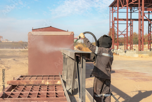 Foto A worker in special clothing is sandblasting a metal building structure at an industrial site